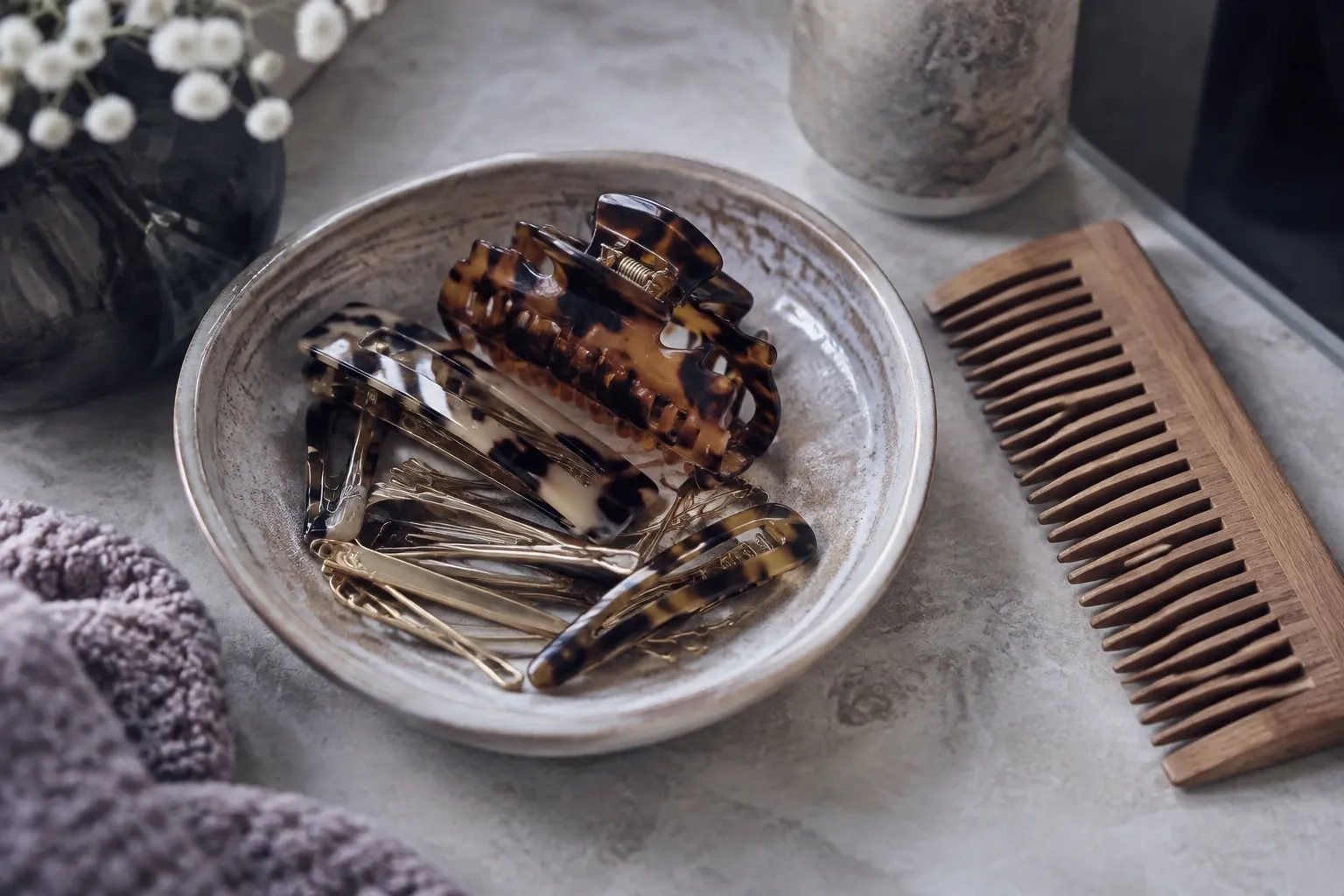 Tortoiseshell hair clips and pins in ceramic dish beside wooden comb and towel
